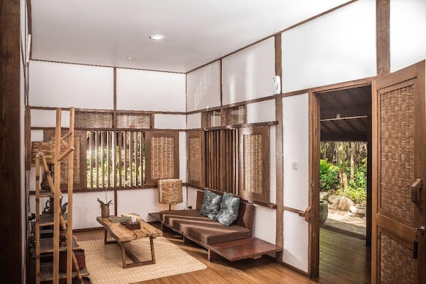A traditional Japanese-style room with tatami flooring, a low wooden bench, a woven basket, and a sliding door leading to an outdoor area.