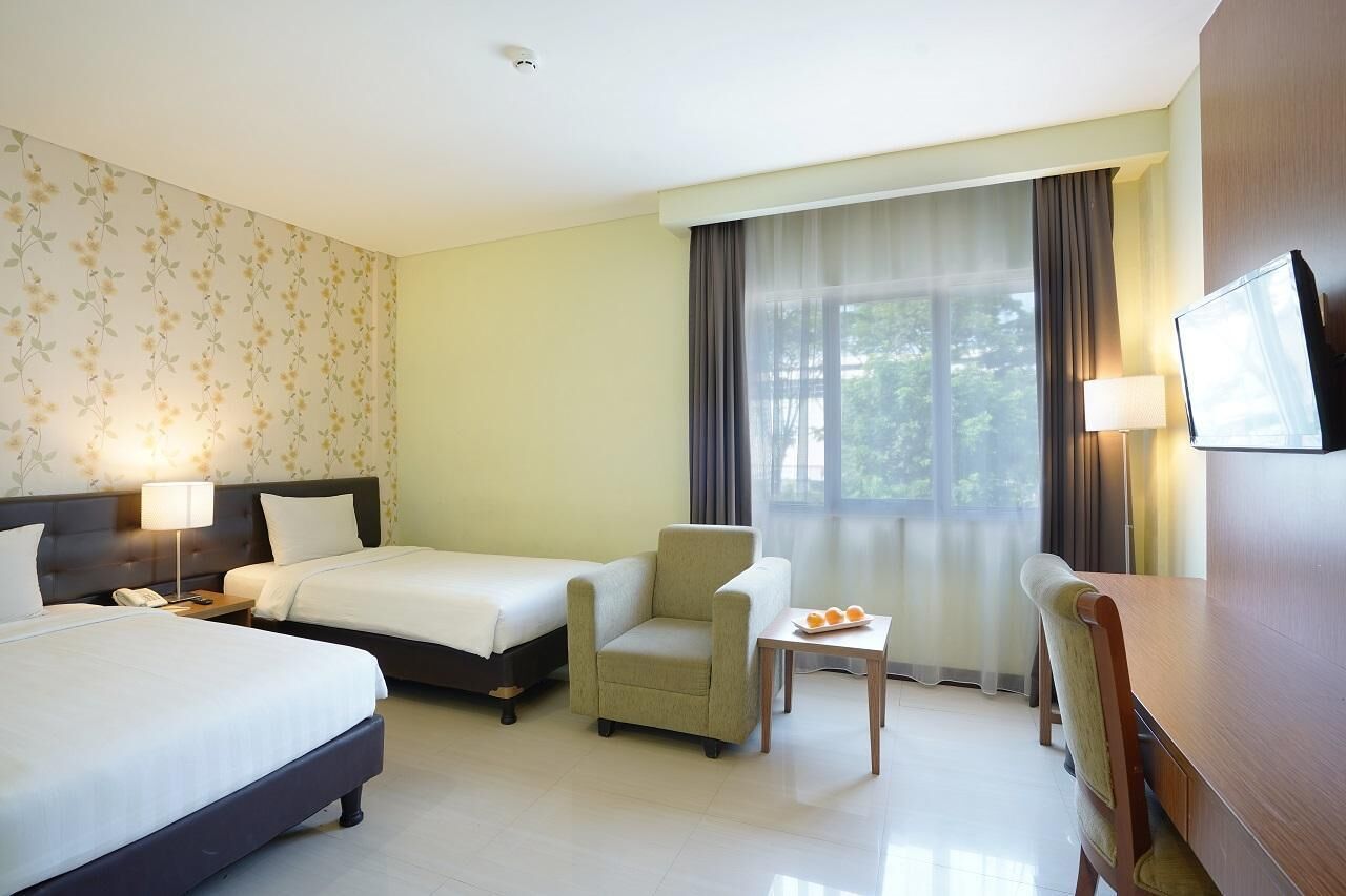 A hotel room with two beds, a chair, a small table with fruit, a TV, and a large window with curtains.