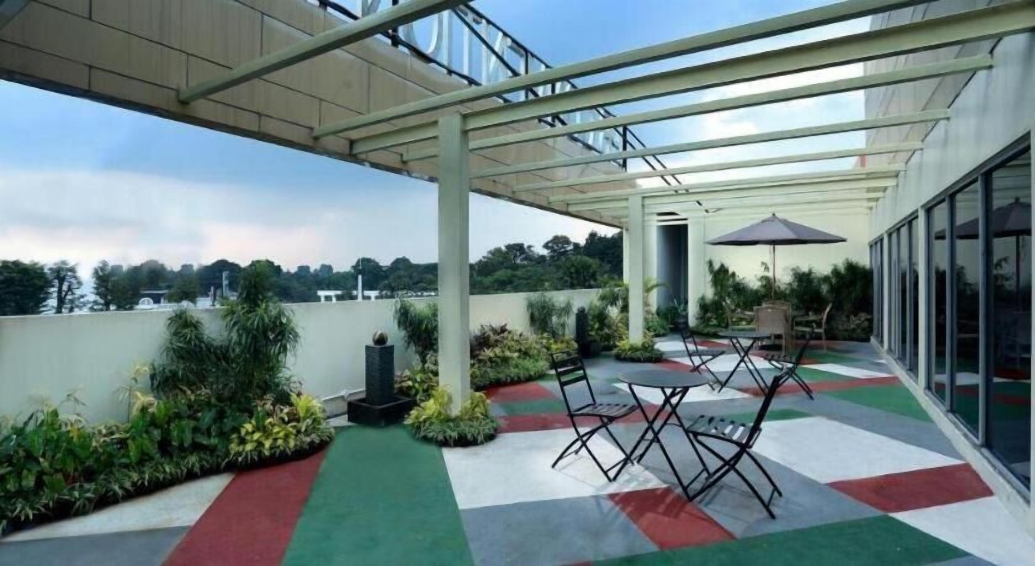 A covered outdoor area with a table and chairs, surrounded by greenery and a view of the sky.