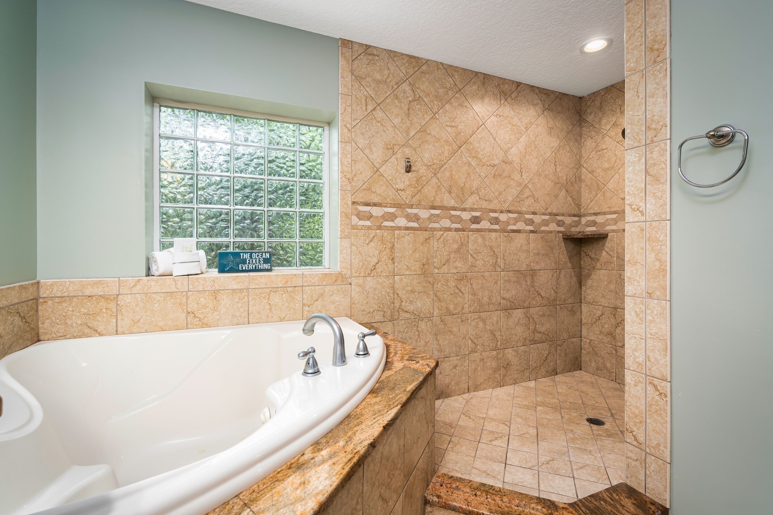 A bathroom with a large bathtub, a shower, and a window providing a view of greenery.
