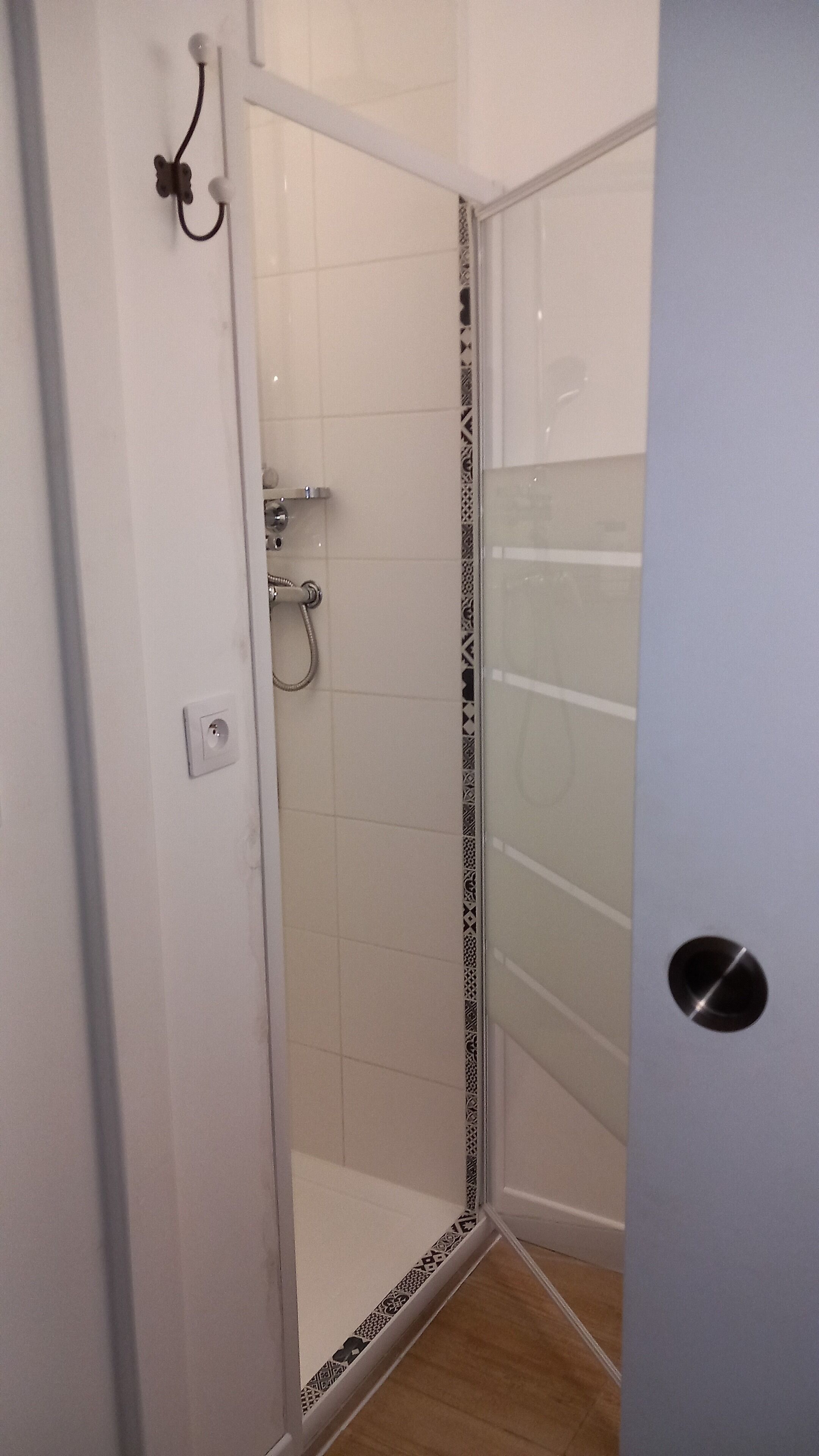 A glass-enclosed shower area with a white tiled wall and a patterned border.