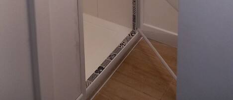 A glass-enclosed shower area with a white tiled wall and a patterned border.