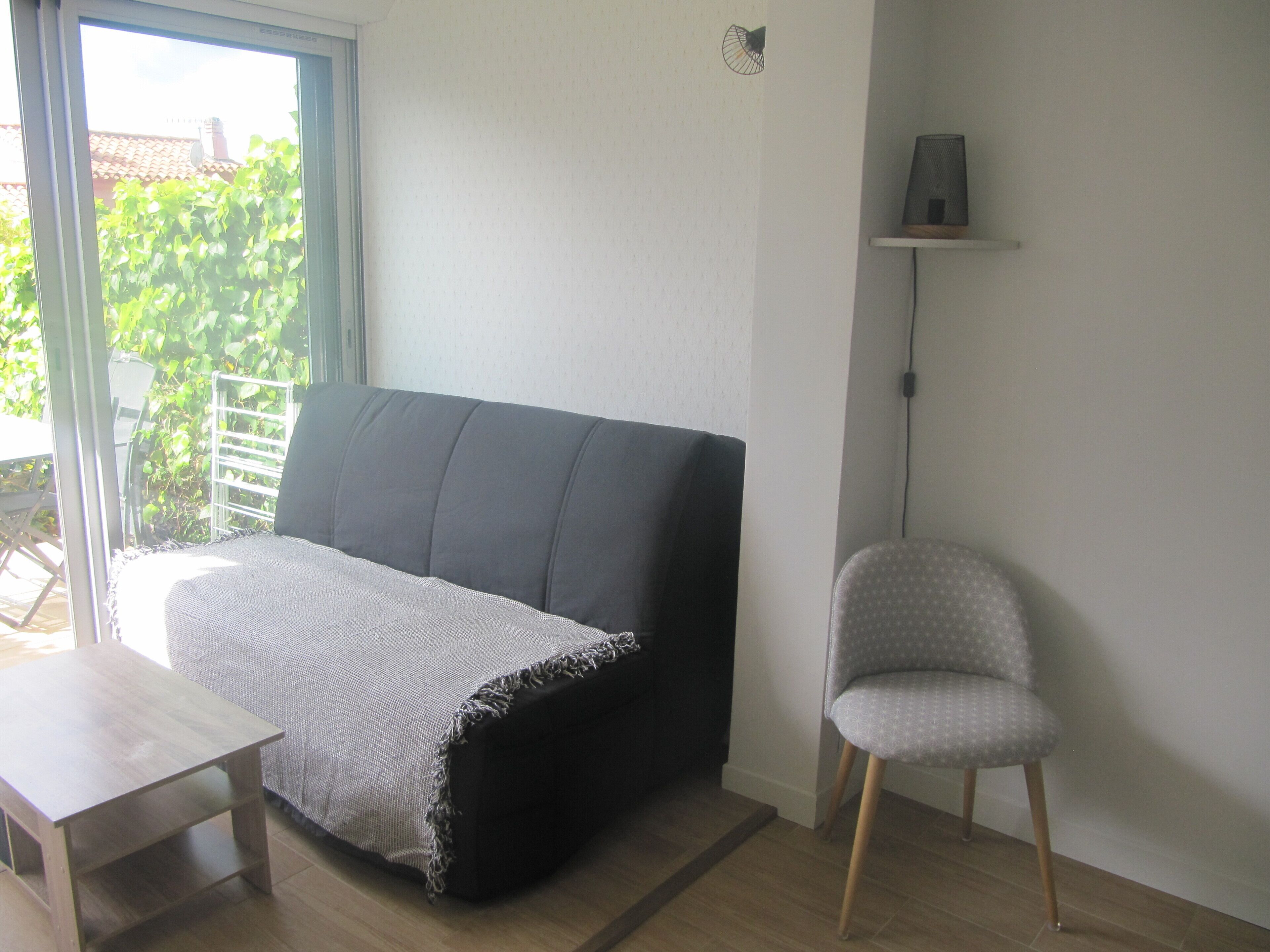 A room with a sofa, a chair, a small table, and a window with a view of greenery.