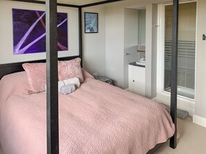 A bedroom with a four-poster bed, a nightstand, a bedside table, a window with blinds, and a door leading to another room.