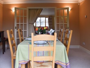 Une salle à manger avec une table dressée pour quatre personnes, des chaises, une fenêtre avec des rideaux et une porte.