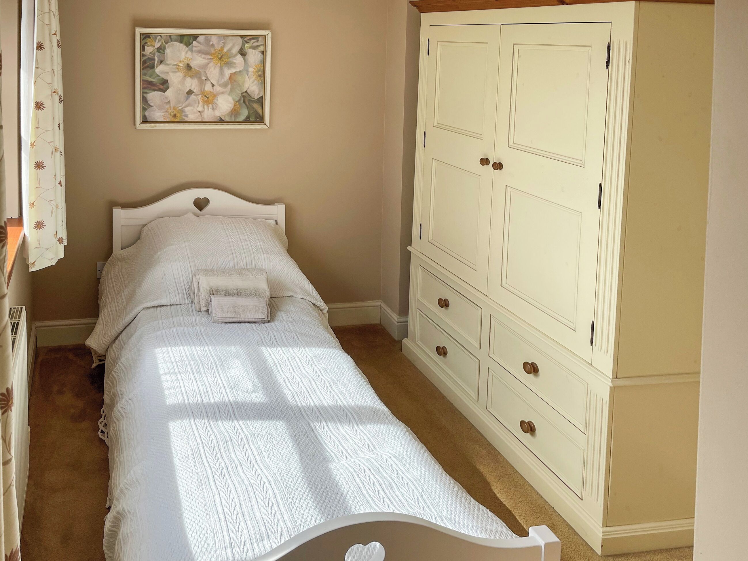 A bedroom with a bed, a wardrobe, a painting, and a window.