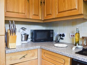 Une cuisine avec des meubles de rangement en bois, un four à micro-ondes, une machine à café et une bouteille d’huile d’olive.