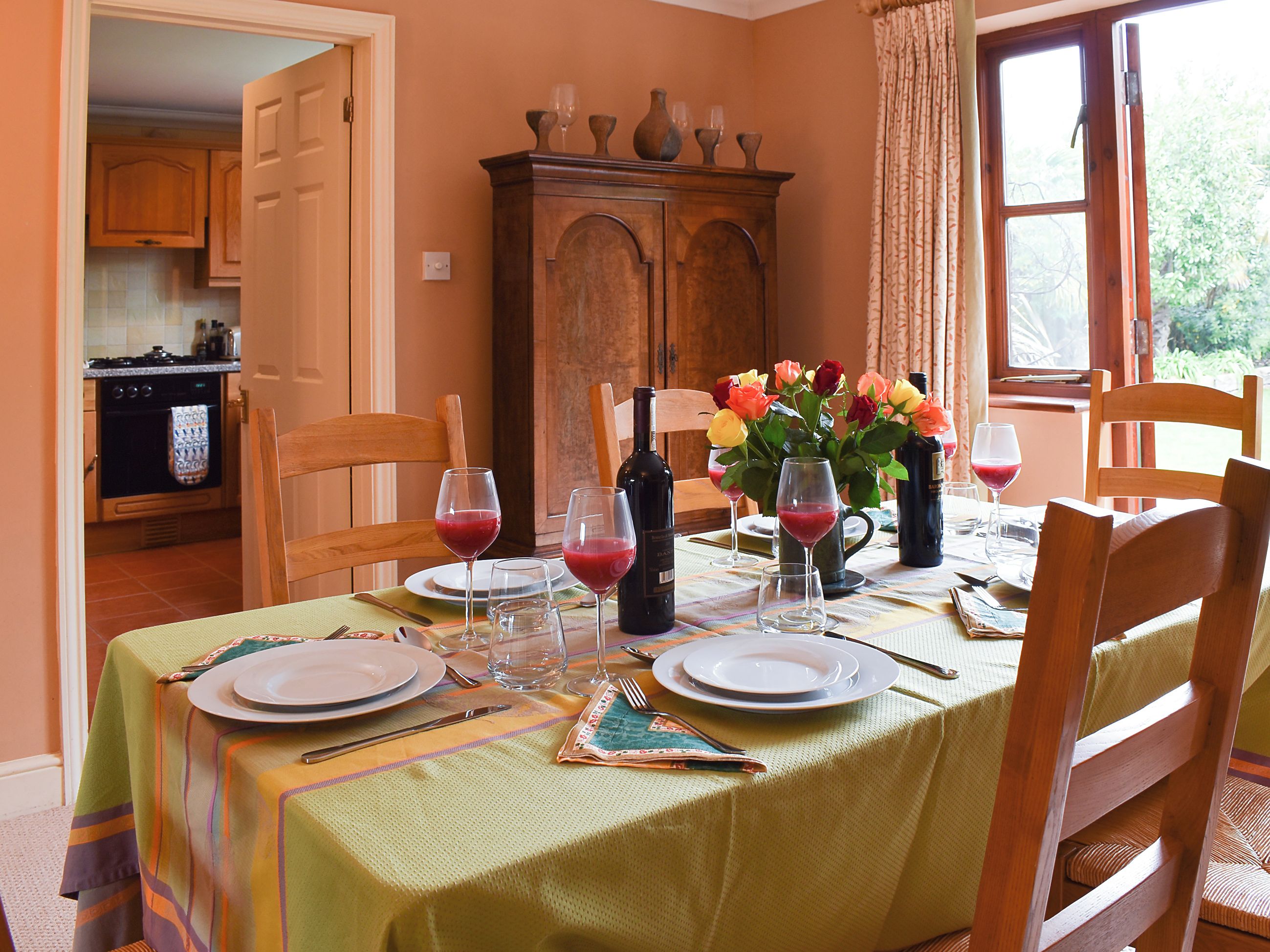 A dining area with a table set for four, a cabinet, and a window with curtains.