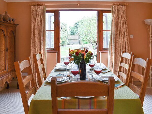 A dining table set for four with chairs, a vase with flowers, and wine glasses.