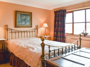A bedroom with a bed, a nightstand, a lamp, a window with curtains, and a painting on the wall.