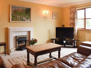 A living room with a fireplace, television, sofa, and a table with flowers.