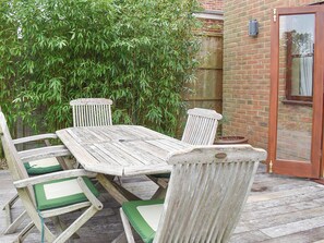 A wooden outdoor table with four chairs, a brick wall, and a bamboo plant in the background.