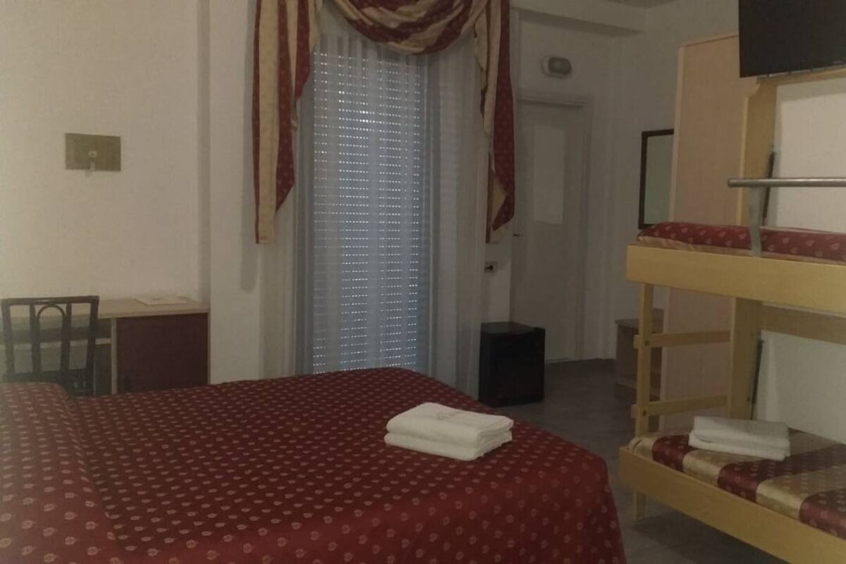Quarto de hotel com cama, escrivaninha e beliche.