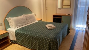 A neatly made bed with a green patterned bedspread and white pillows, a wooden nightstand, a small wooden cabinet, and a mirror on the wall. - Casa Major Hotel & Appartamenti Cervia (Cervia)