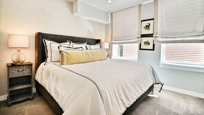 Une chambre à coucher avec un grand lit, une table de chevet, une lampe et une fenêtre avec des stores.