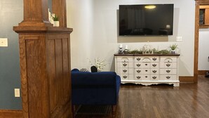 Uma sala de estar com piso de madeira, um sofá azul, um armário branco com gavetas e uma TV de tela plana fixada na parede.