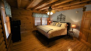 Een slaapkamer in een houten hutje, met een bed, een plafondventilator, een nachtkastje en een lamp.