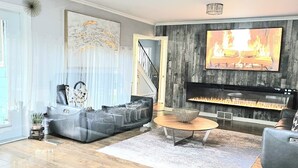 A modern living room with a fireplace, a large TV, and a staircase leading to another level. - ***OASIS*** (Ingersoll)