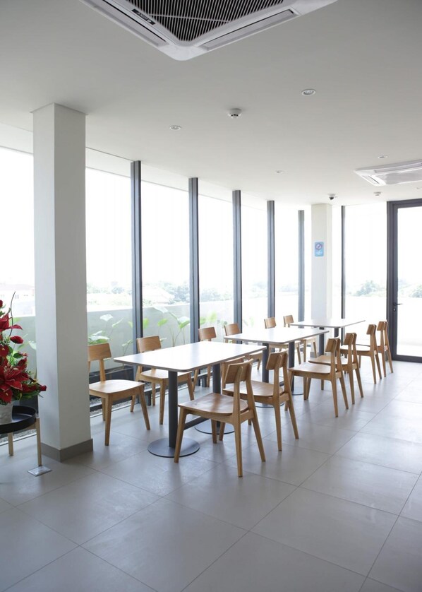 A modern dining area with large windows, white walls, and wooden chairs. - Citrip Hotel Simpang Lima (Semarang)
