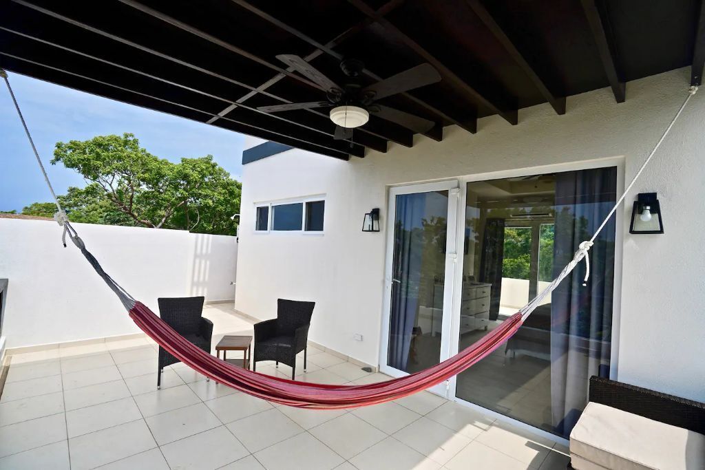 A covered patio with a hammock, two chairs, and a sliding glass door leading to a balcony.