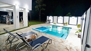 Ein Swimmingpool mit Liegestühlen und einem kleinen Tisch, umgeben von Steinfliesen und einem weißen Gebäude.