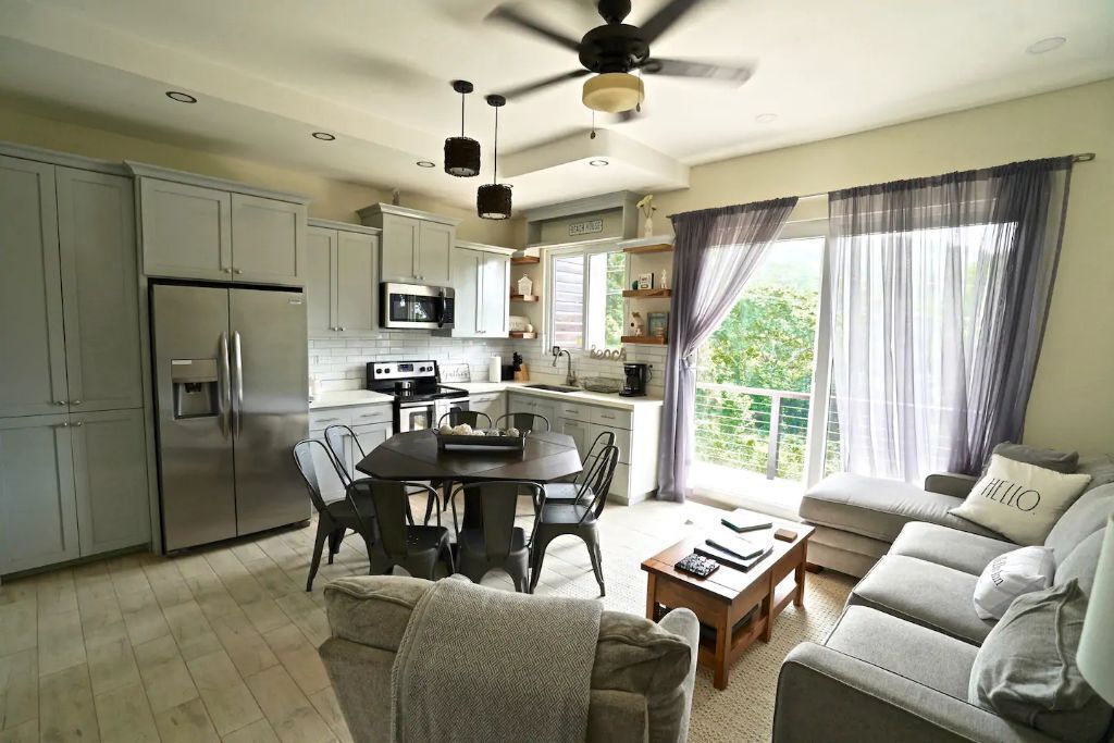 Una cocina moderna con electrodomésticos de acero inoxidable, un comedor con una mesa redonda y sillas, y una sala de estar con un sofá y una mesa de centro.