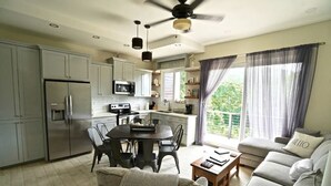 Eine moderne Küche mit Edelstahlgeräten, ein Essbereich mit rundem Tisch und Stühlen sowie ein Wohnzimmer mit Sofa und Couchtisch.