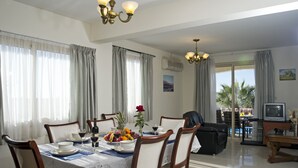A dining area with a table set for four, a television, and a balcony with a view of palm trees.
