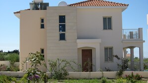 A two-story building with a tiled roof, a balcony on the upper floor, and a small garden area with various plants and flowers.