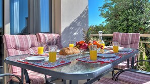 A dining table with a glass top, surrounded by striped cushioned chairs, set with plates, glasses, a loaf of bread, and a fruit bowl.