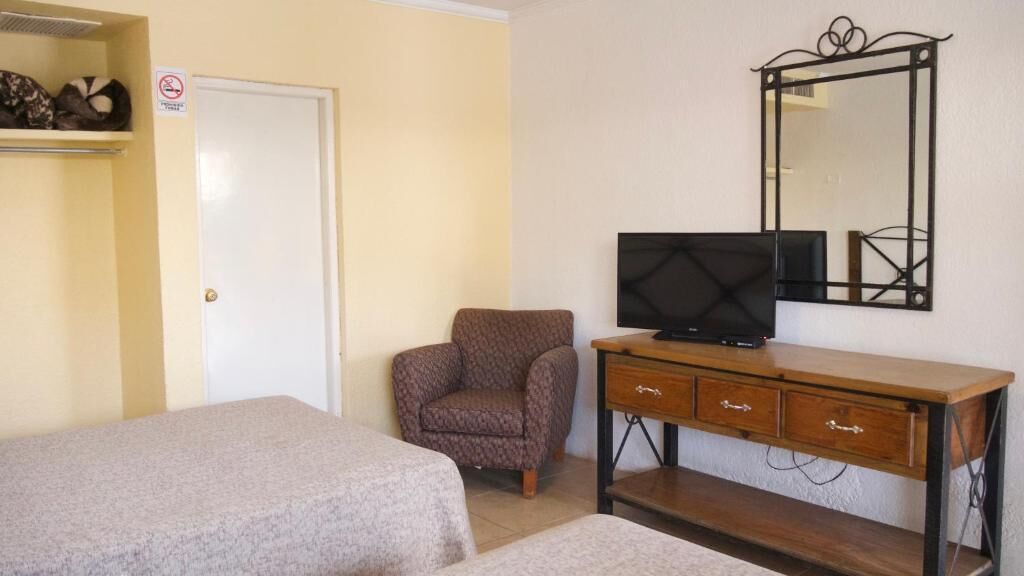 Un dormitorio con dos camas, una silla, un televisor y un aparador.