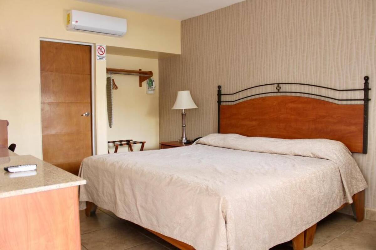 A hotel room with a bed, a desk, a lamp, and an air conditioning unit.