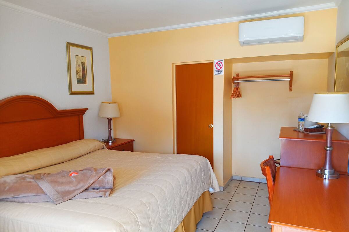 A hotel room with a bed, bedside table, lamp, wardrobe, and a mirror.