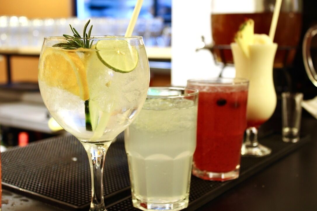 A bar area with various drinks, including a lime and rosemary cocktail, a white beverage, and a red drink.