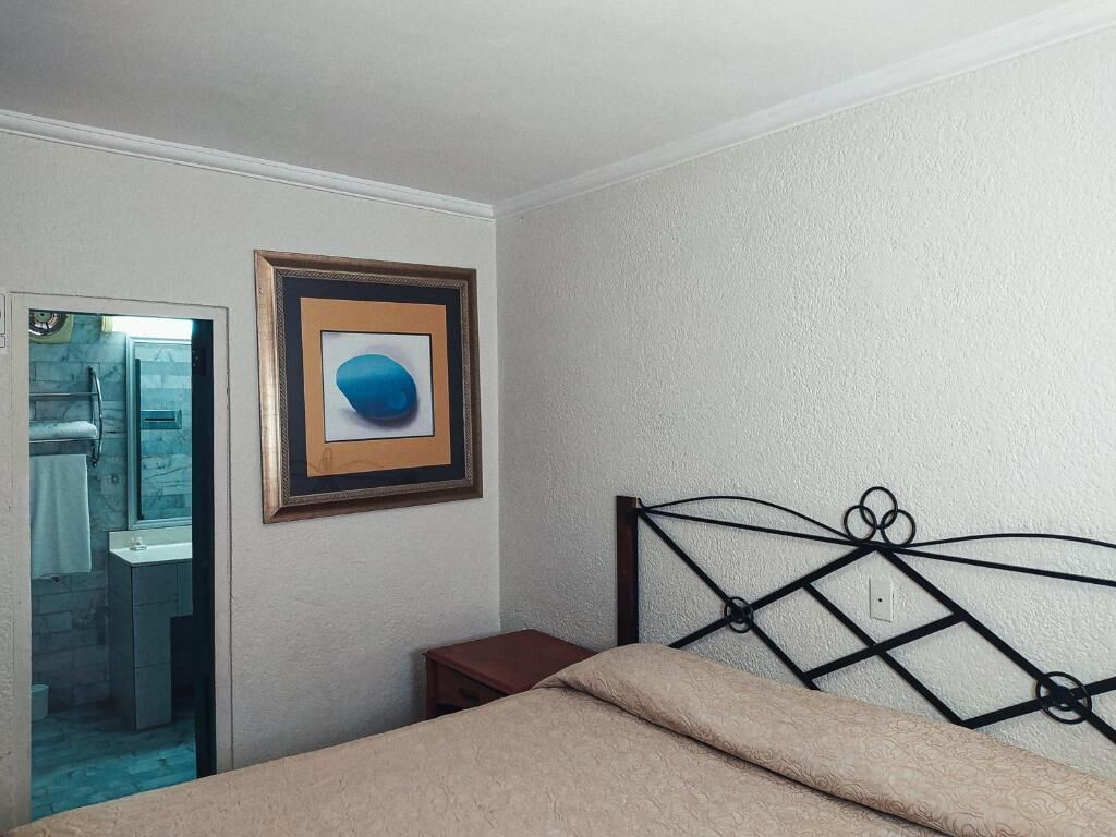 A bedroom with a bed, a framed picture on the wall, and a bathroom visible through an open door.