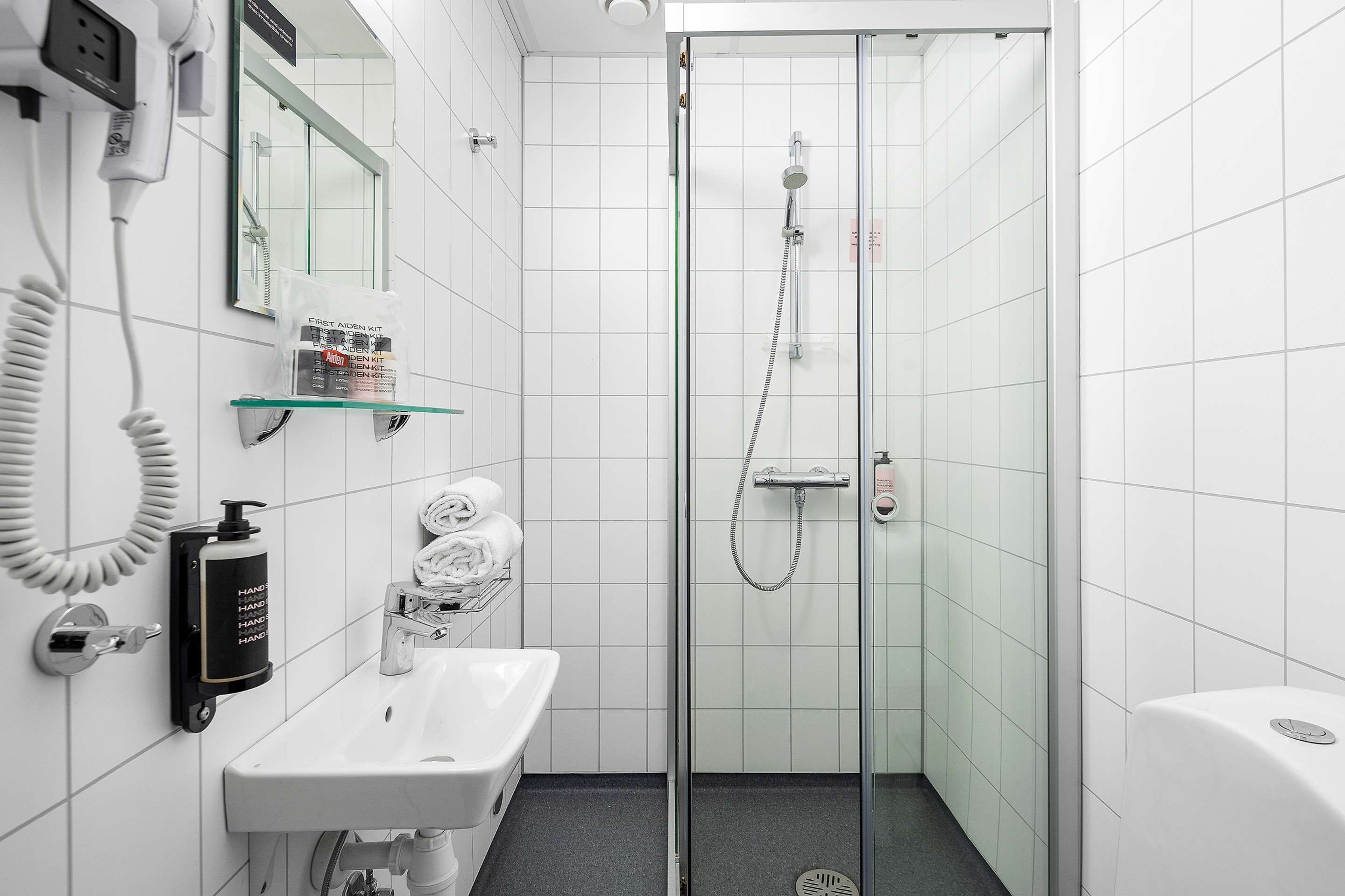 Une salle de bain moderne avec une douche à parois de verre, un lavabo blanc et un sèche-mains.