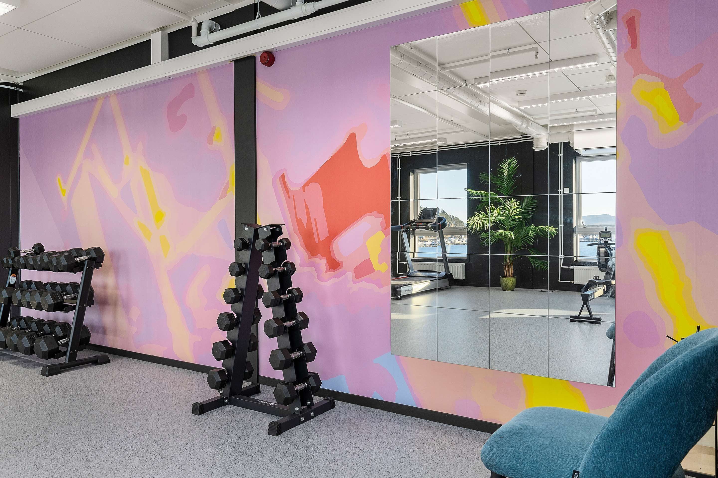 Uma academia com equipamentos de ginástica e um espelho grande refletindo o ambiente.