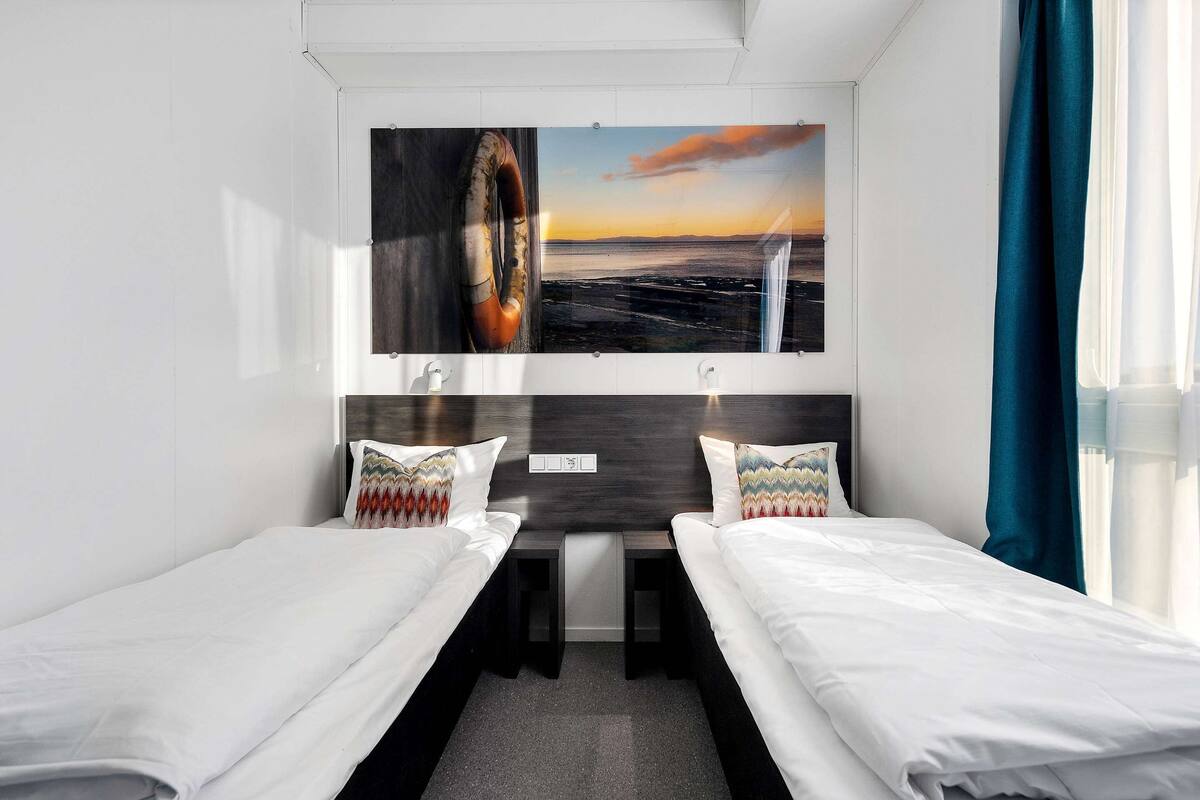 A hotel room with two single beds, a small table, and a large window with curtains.