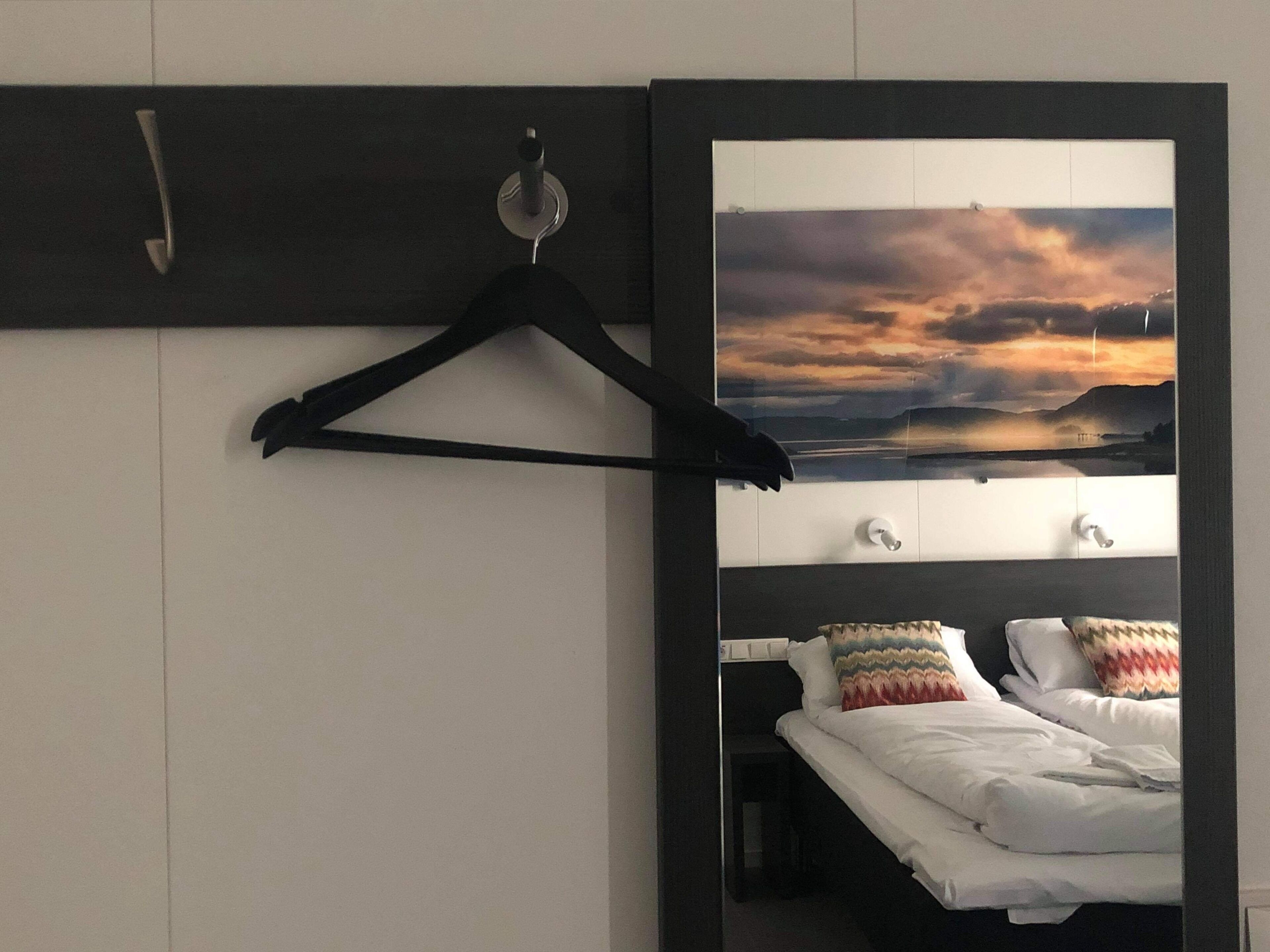 Una habitación de hotel con una cama, una mesita de noche, un espejo y un televisor instalado en la pared.