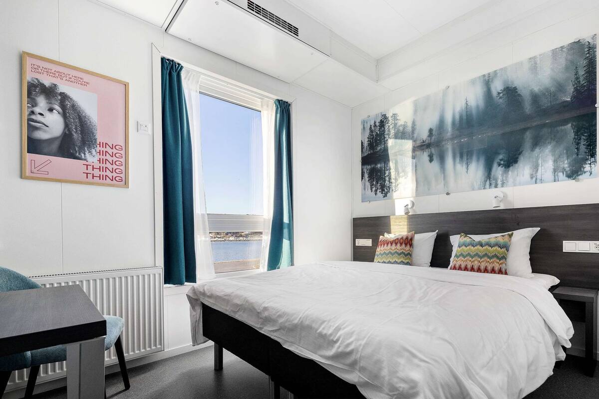 A modern hotel room with a large bed, a view of the sea, and a painting on the wall.