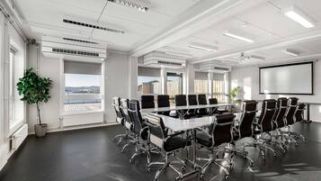 Une salle de conférence avec une longue table, des chaises noires et un écran de projection.
