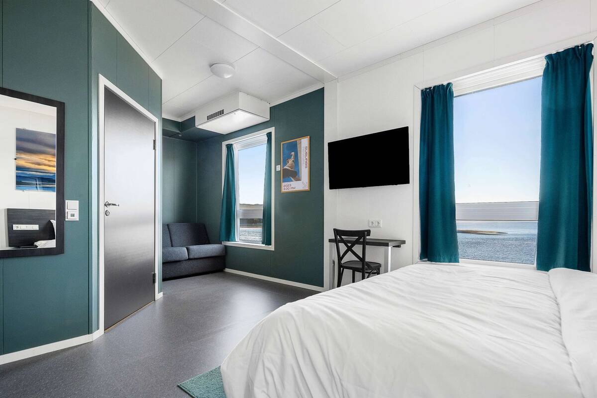 A hotel room with a bed, a desk, a chair, a TV, and a window with curtains.