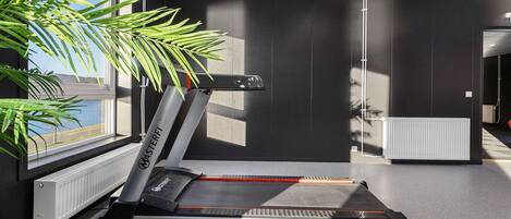 A treadmill in a modern room with a large window, a radiator, and a plant.