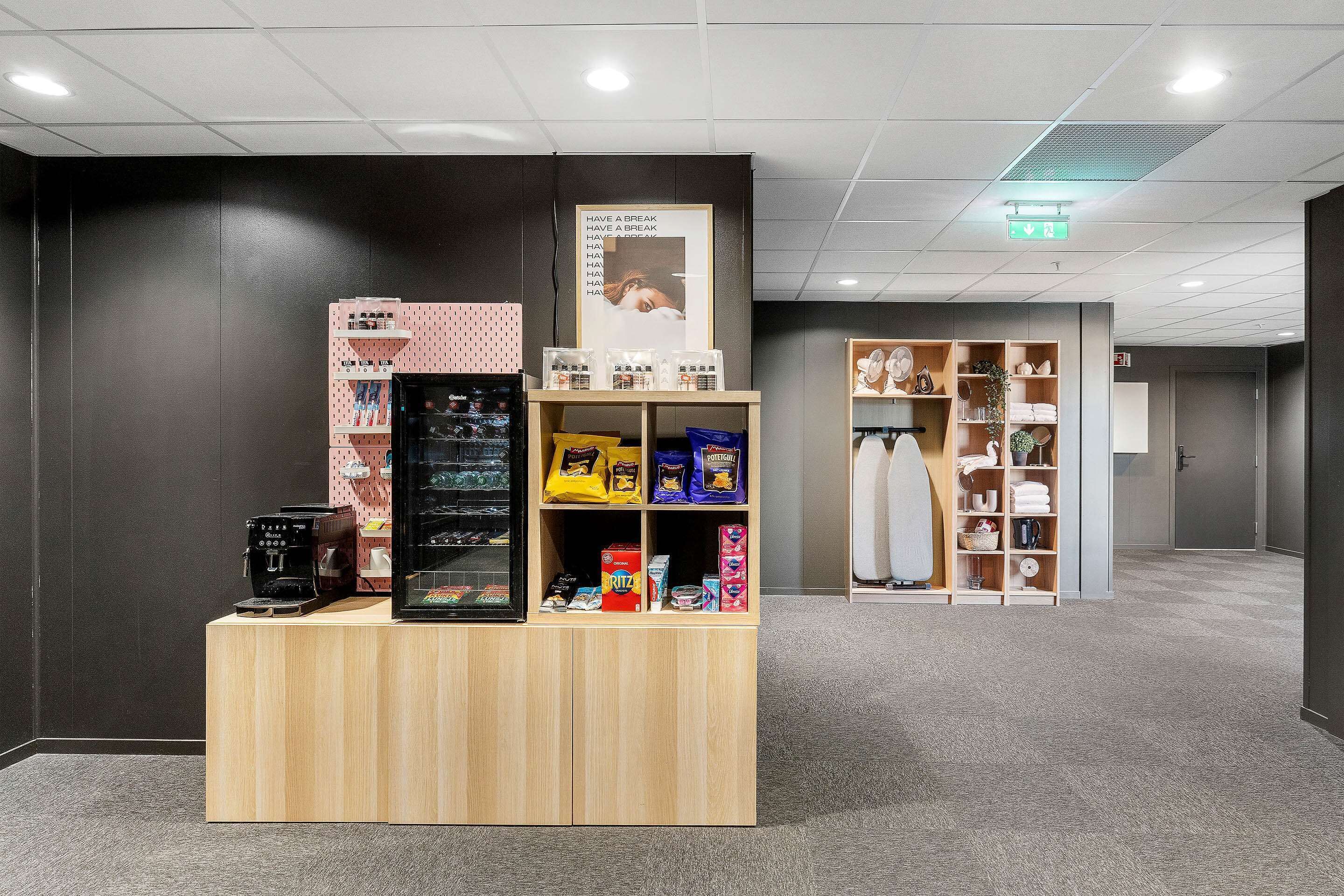 Uma área de recepção de hotel com uma máquina de café, distribuidores de lanches e um cartaz na parede.