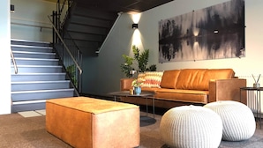 A modern living room with a staircase, a sofa, ottomans, and a large abstract painting. - Aiden By Best Western Trondheim Airport (Stjordal)