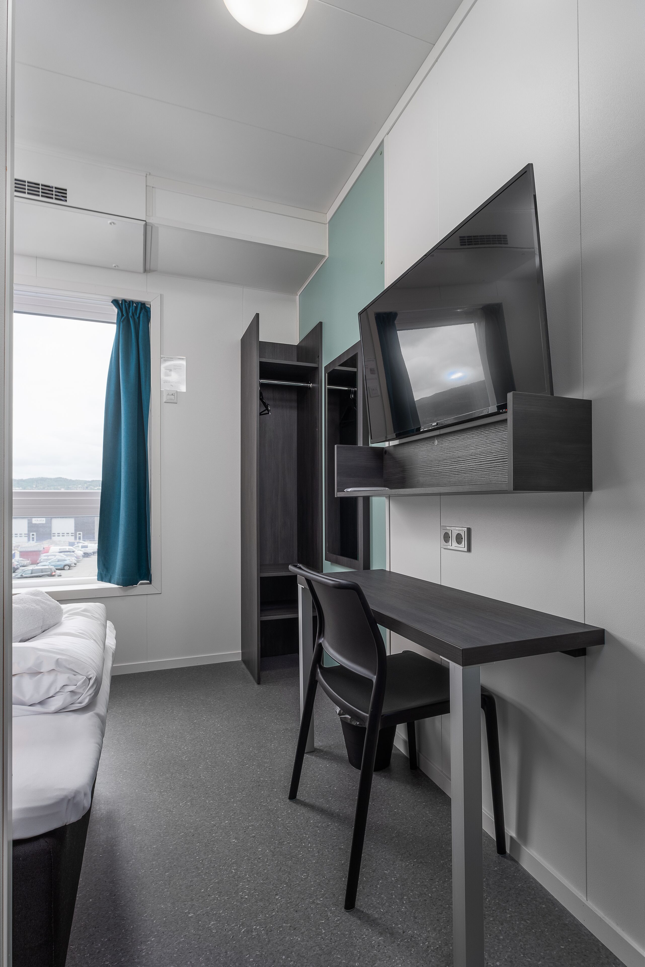 A compact room with a bed, a desk, and a TV mounted on the wall.