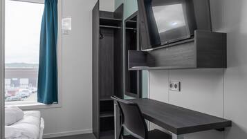 A compact room with a bed, a desk, and a TV mounted on the wall.