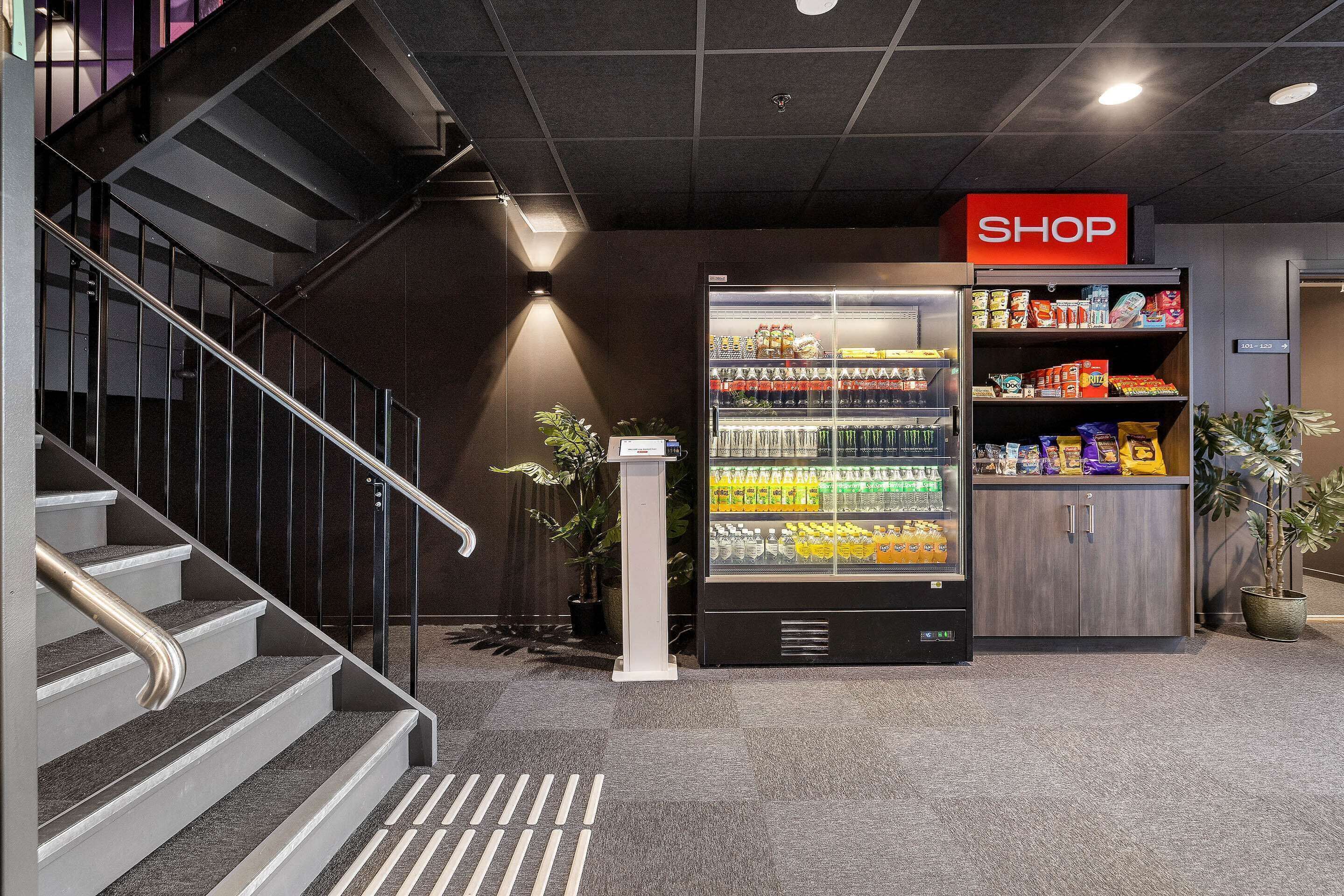 A modern indoor setting with a staircase, a vending machine, and a 'SHOP' sign.