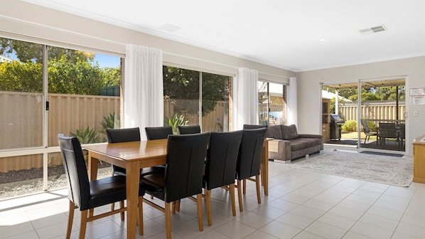 Tilava huone, jossa on ruokapöytä ja -tuolit, sohva sekä liukuovella varustettu lasiterassi, joka johtaa takapihalle.