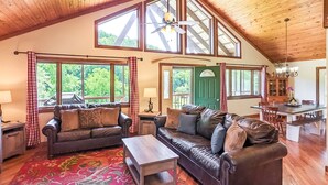 A spacious living room with leather sofas, a coffee table, and a large window overlooking greenery.